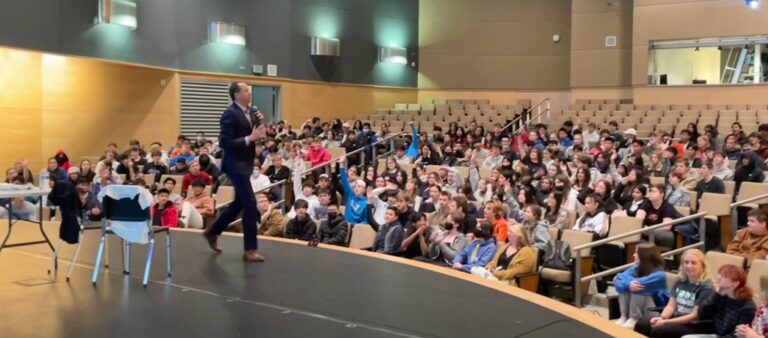 Students raising their hands during an interactive middle and high school respect assembly in a school auditorium.